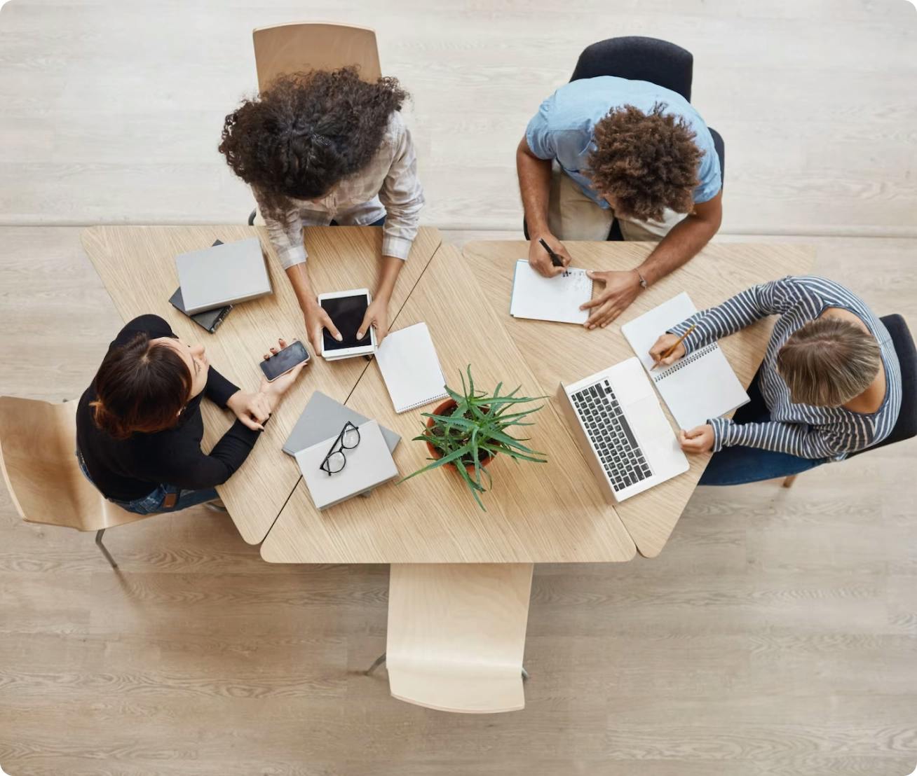 Imagem vista de cima uma mesa com quatro pessoas trabalhando